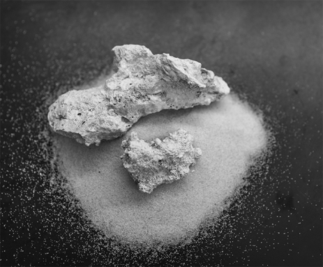 Two pieces of rock sit on top of a pile of sand. The rocks were created by breaking down water-saturated sand with low-voltage electricity.